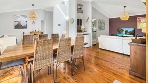A spacious living area with a wooden dining table, wicker chairs, a white sofa, and a television. - Riverside 3-Bed Townhouse with Spacious Deck (Mossy Point)