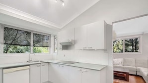 A modern kitchen with white cabinetry, a built-in oven, and a window with blinds. - Riverside 3-Bed Townhouse with Spacious Deck (Mossy Point)