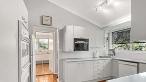 A modern kitchen with white cabinetry, a built-in microwave, and a wooden floor. - Riverside 3-Bed Townhouse with Spacious Deck (Mossy Point)