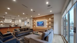 Ett modernt vardagsrum med en stor platt-TV, soffor och en köksdel.