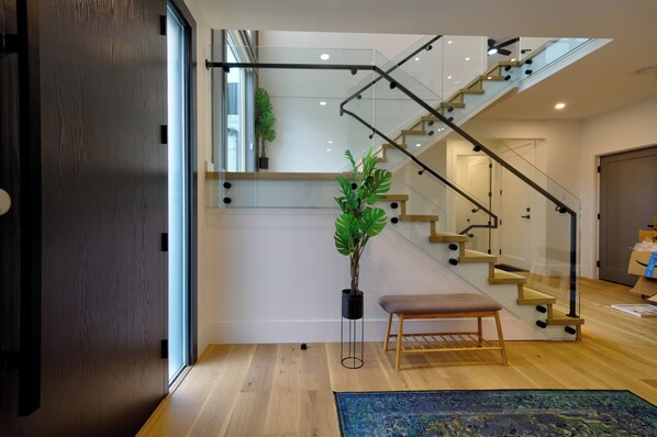 Een modern interieur met een houten vloer, een glazen trap, een bankje en een kamerplant.