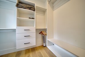 Een witte kast met open planken en lades, een kledingroede en een vloerventilator.