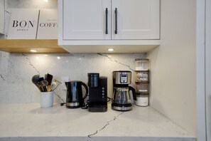 Een keuken met een koffiezetapparaat, een waterkoker en een suikerpot op het aanrecht.