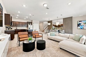 Ein modernes Wohnzimmer mit einer Couch, zwei Sesseln, einem Couchtisch und einer Küche im Hintergrund.