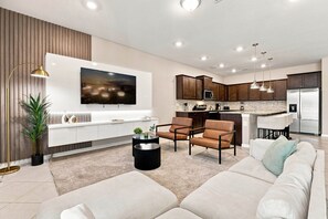 Un salon moderne avec un canapé, des fauteuils, une table basse et un téléviseur fixé au mur.