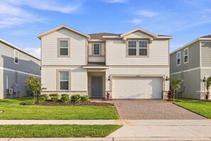 A two-story residential building with a garage, a front door, and a driveway leading to the entrance. - Stunning 10 Bed Home with Themed Rooms, Pool (Clermont)