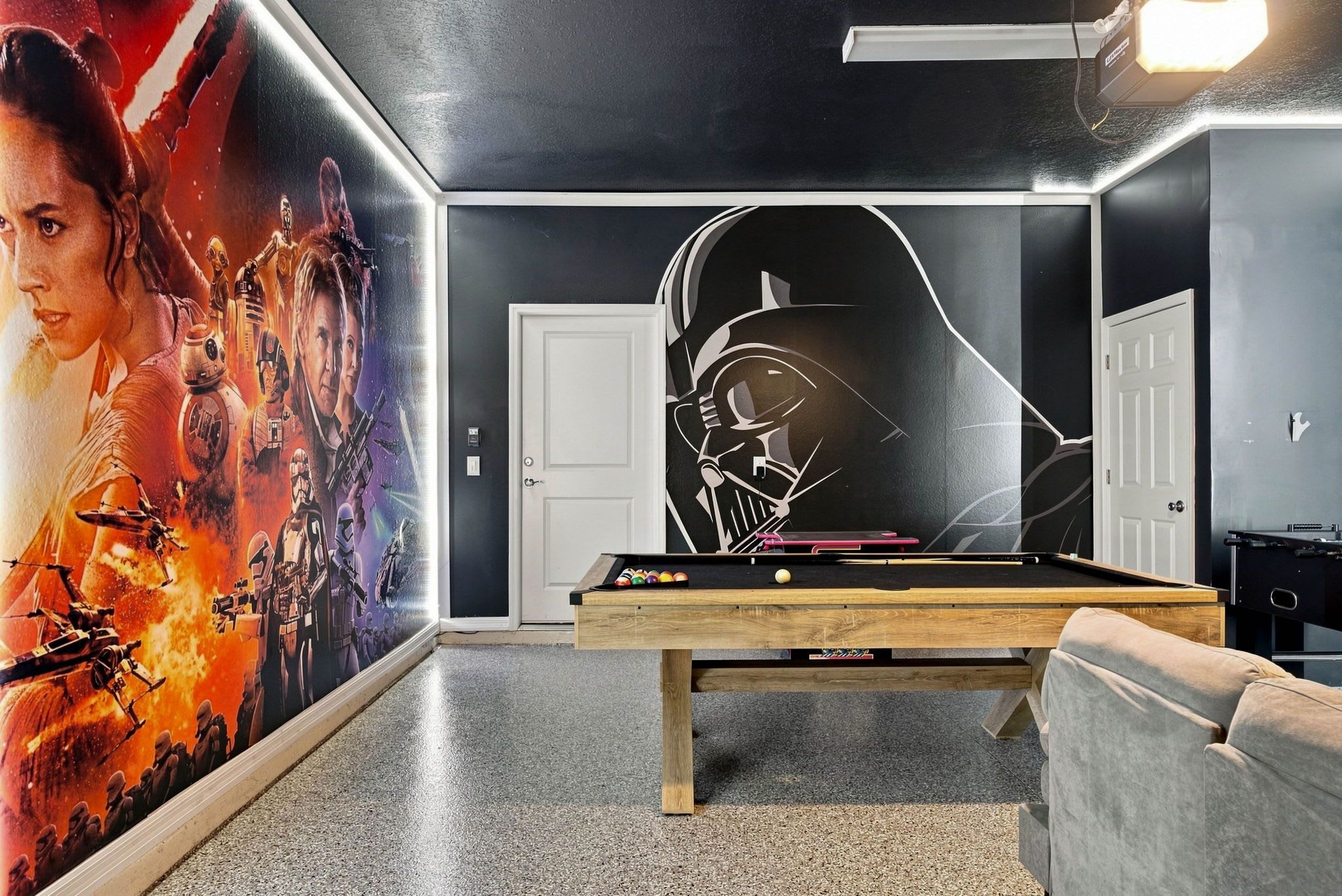 A room with a pool table, a sofa, and a wall with a Star Wars-themed mural.