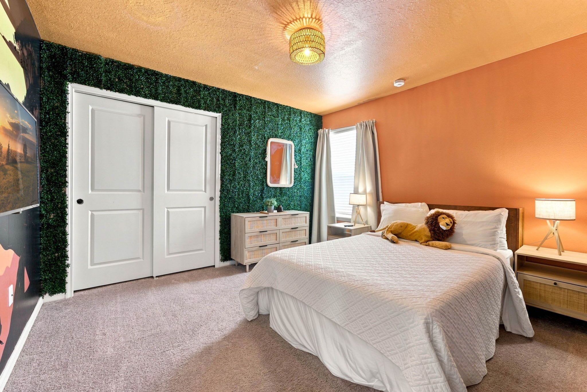 A bedroom with a bed, a nightstand, a dresser, a mirror, and a wall with a green leafy texture.