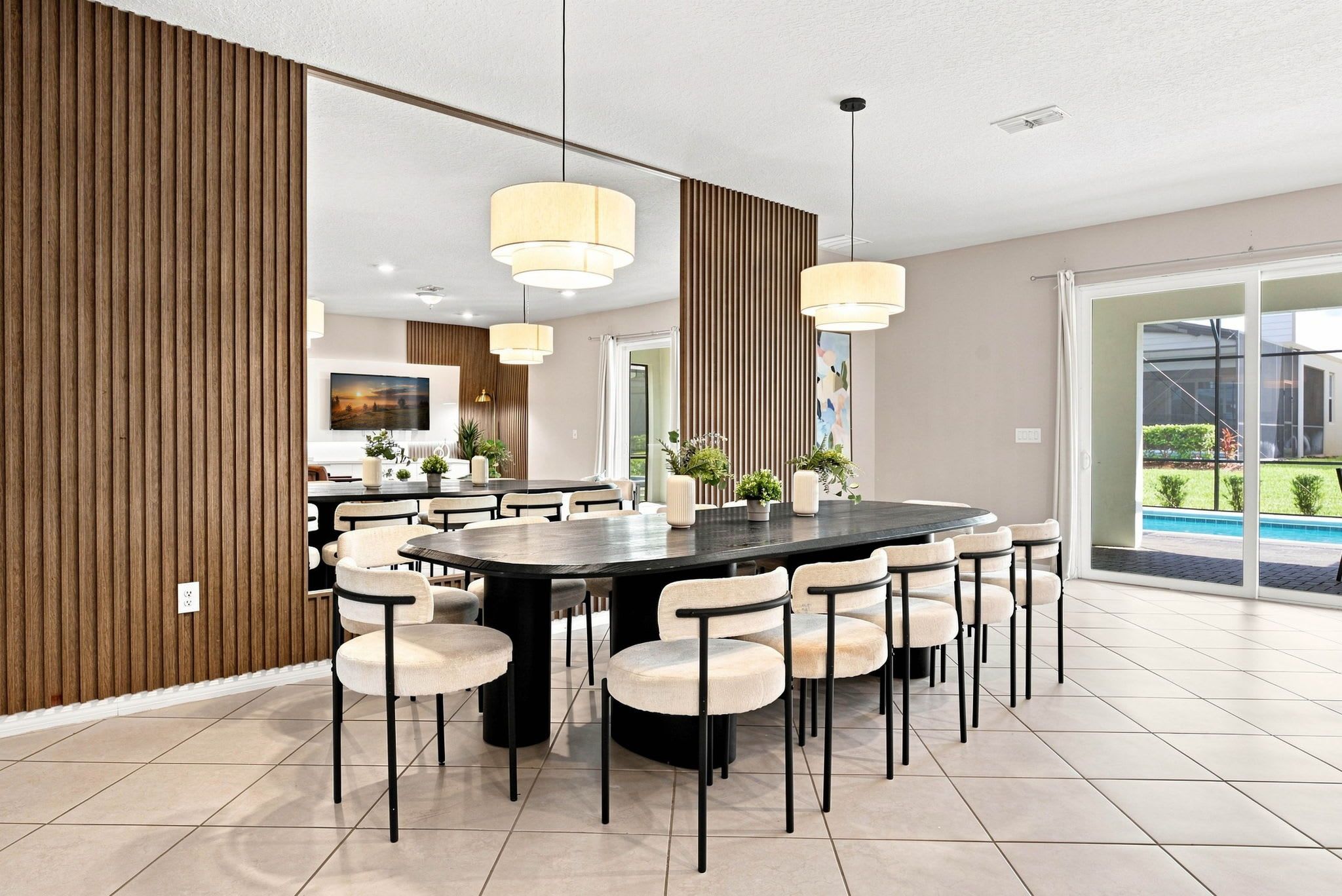 A modern dining area with a round table, multiple chairs, pendant lighting, and a view of a swimming pool.