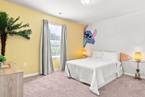 Une chambre à coucher comprenant un lit, une table de chevet, une lampe, un élément de décoration murale et une fenêtre avec des rideaux.