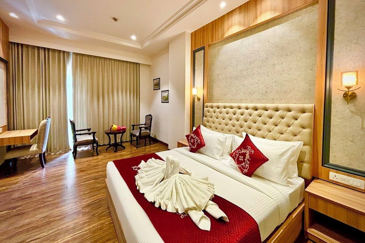 A hotel room with a large bed, two chairs, a desk, and a large mirror.