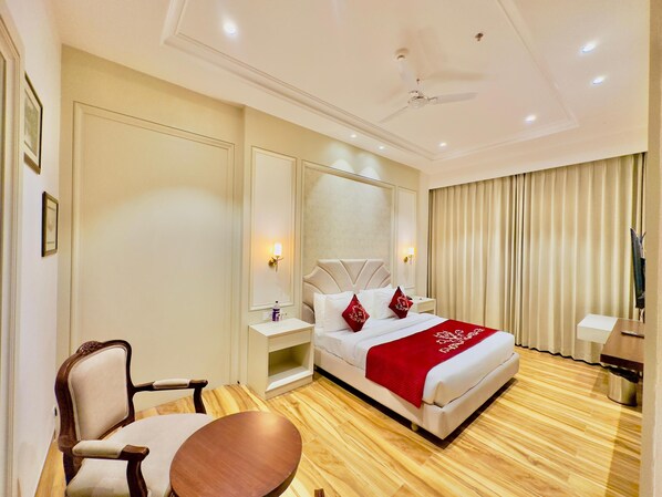 A hotel room with a bed, a chair, a small table, a ceiling fan, and a large mirror. - HOTEL SUKH FARM (Sangrur)