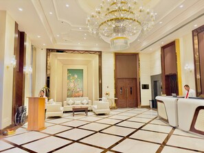 A hotel lobby with a reception desk, seating area, and a large chandelier. - HOTEL SUKH FARM (Sangrur)