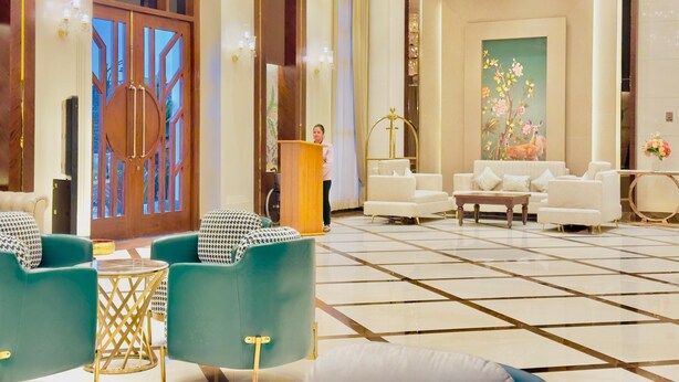 A spacious lobby with a large chandelier, a reception desk, and a seating area with green and white chairs. - HOTEL SUKH FARM (Sangrur)