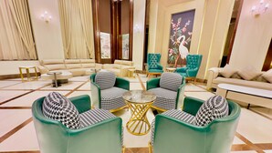 A spacious lobby with a sectional sofa, houndstooth patterned chairs, a round table, and a large painting of a swan. - HOTEL SUKH FARM (Sangrur)
