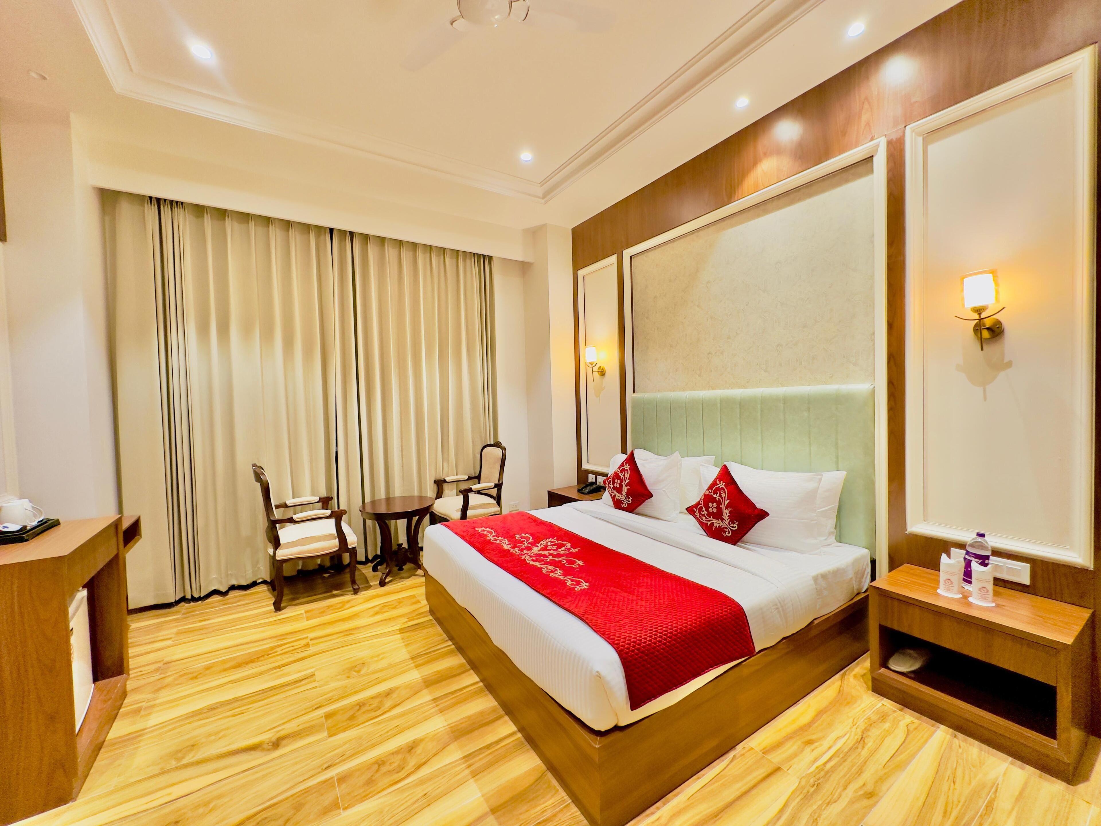 A hotel room with a large bed, a desk, two chairs, a small table, and a large mirror.