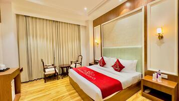 A hotel room with a large bed, a desk, two chairs, a small table, and a large mirror.