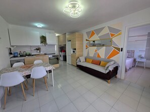 A modern kitchen with white cabinets, a dining table with chairs, a sofa, and a decorative wall.