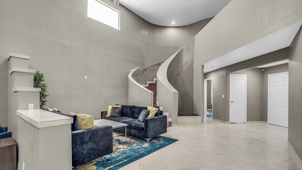 A spacious living area with a curved staircase, a dark grey sofa set, and a blue patterned rug. - Grand Casa • 8bdr • Strip Views• 21 Beds • Free Spa Heat • Basketball • Events (Las Vegas)