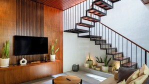 Una sala de estar moderna con una pared de madera, un televisor de pantalla plana, una mesa de centro redonda y una escalera con barandilla de metal.