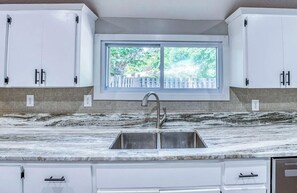 A kitchen with white cabinets, a marble countertop, a stainless steel sink, and a window with a view of trees. - Beautiful Artistic Dog-Friendly Farmhouse Near Asheville, Cozy, Nature & Relax (Candler)