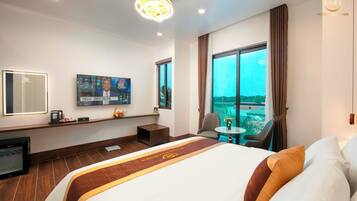 Habitación de hotel con una cama grande, un televisor montado en la pared, una mesita con una silla y un ventanal con vistas a la ciudad.