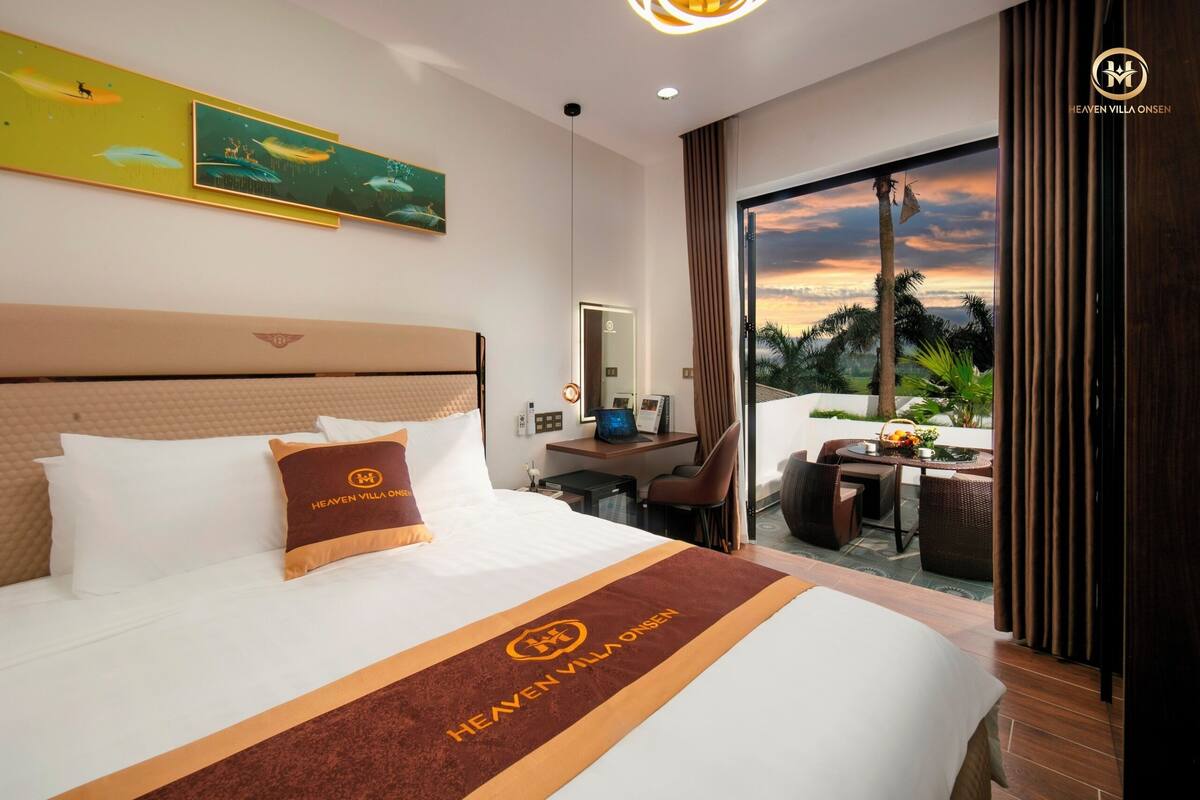 A hotel room with a bed, a desk, and a view of the sunset.