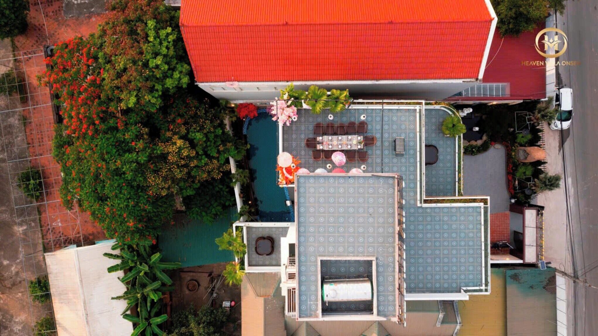 An aerial view of a building with a red roof, a swimming pool, and a patio area with seating.