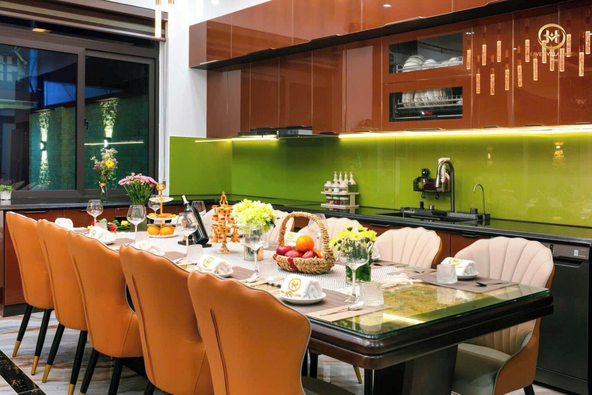 A modern dining area with a glass table, orange chairs, and a green backsplash.