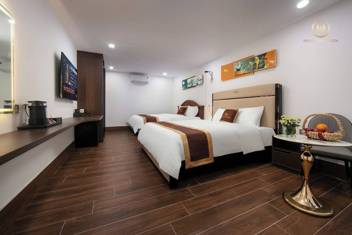 A hotel room with two beds, a small table with a vase, and a TV on the wall.