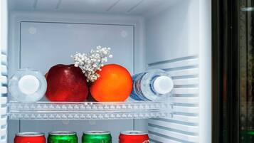 A refrigerator with a clear shelf, containing a bottle of water, an apple, an orange, and three cans of Coca-Cola.