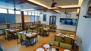 Uma sala de jantar com várias mesas e cadeiras, ventiladores no teto e uma televisão na parede.