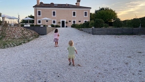 A large building with a symmetrical facade, a gravel driveway, and a paved patio area with umbrellas. - Manor in Marche With Pool Near Adriatic (Monsano)