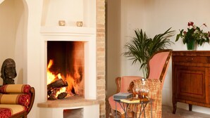 A cozy living room with a fireplace, a comfortable armchair, a wooden cabinet, and a potted plant. - Manor in Marche With Pool Near Adriatic (Monsano)