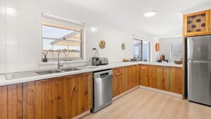 A modern kitchen with wooden cabinets, stainless steel appliances, and a dishwasher. - The Castle - Pet Friendly - Absolute Beachfront (Culburra Beach)