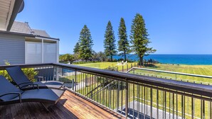 A deck with outdoor furniture, a view of the ocean, and a lawn with trees.