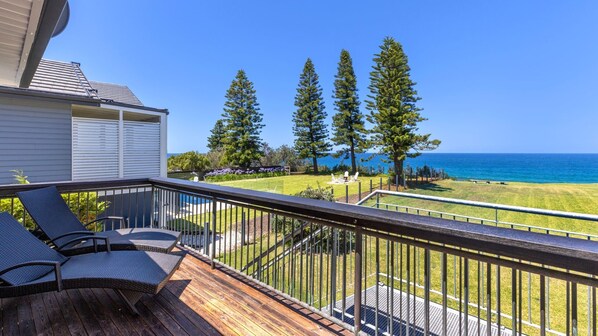 Une terrasse dotée de mobilier d’extérieur, offrant une vue sur l’océan et donnant sur une pelouse agrémentée d’arbres.