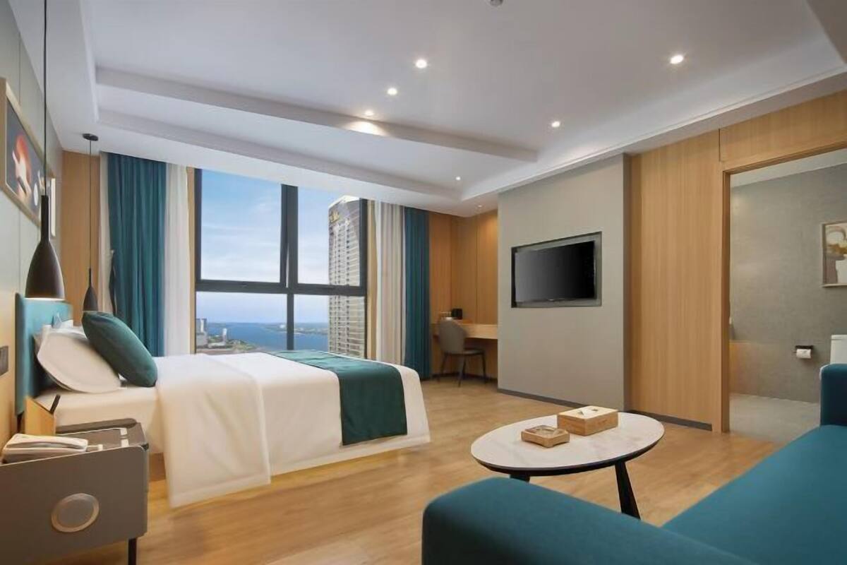 Een moderne hotelkamer met een bed, een bureau, een televisie en uitzicht op de stad.