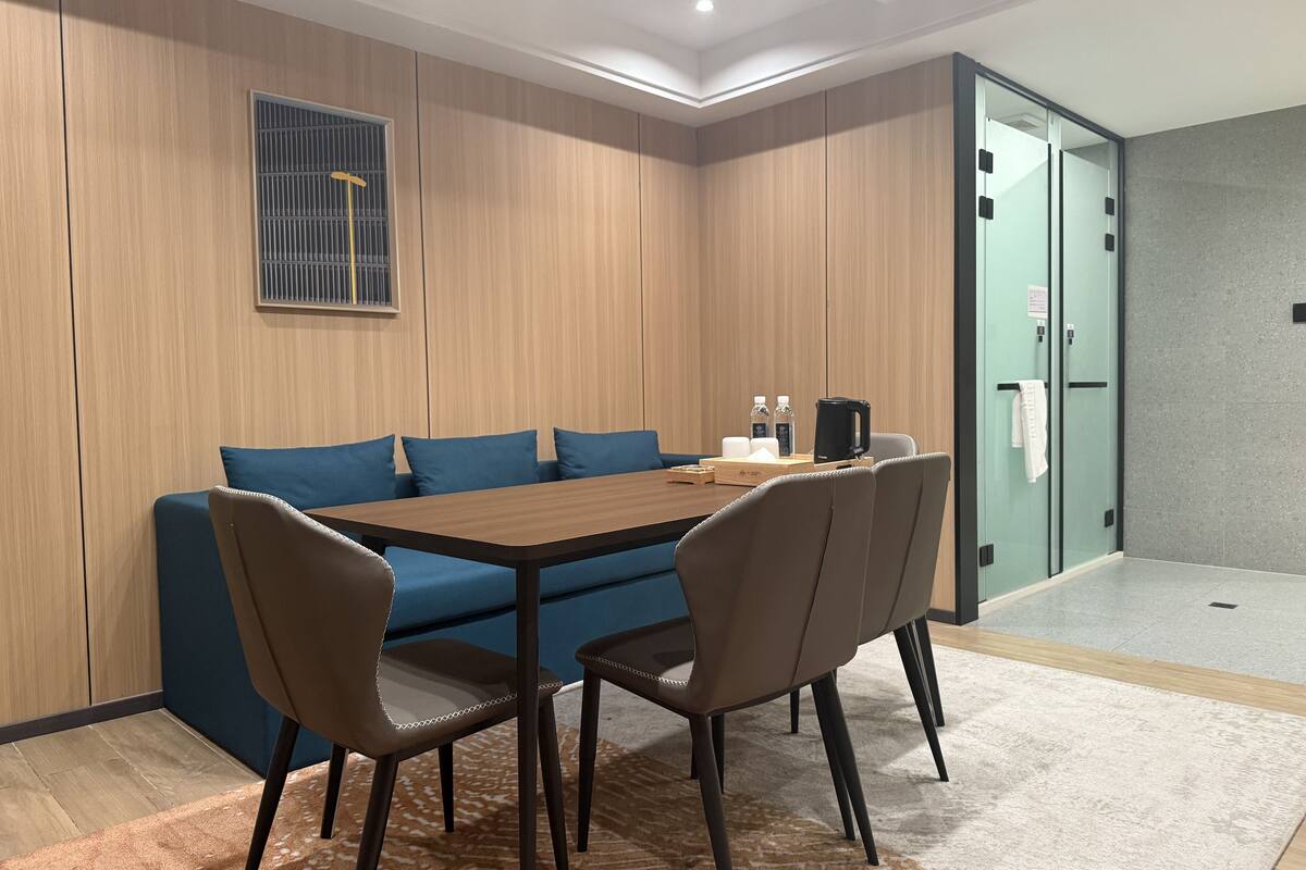 Een congresruimte met een wand van houten panelen, een blauwe bank, een houten tafel en zes stoelen.