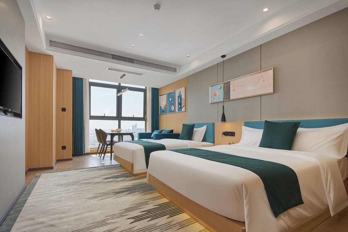 Een hotelkamer met twee bedden, een zithoek en een groot raam met uitzicht op de stad.