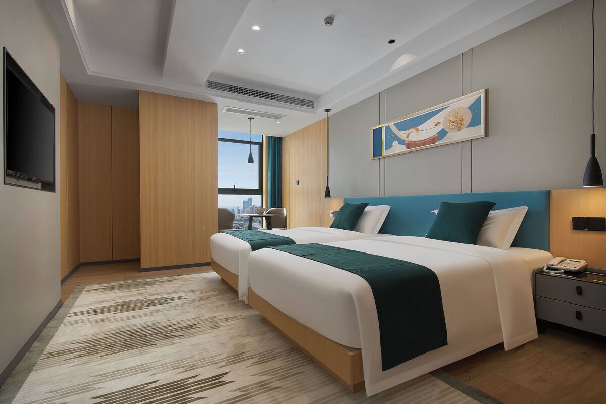 Een moderne hotelkamer met twee bedden, een flatscreen televisie, een schilderij en uitzicht over de stad.
