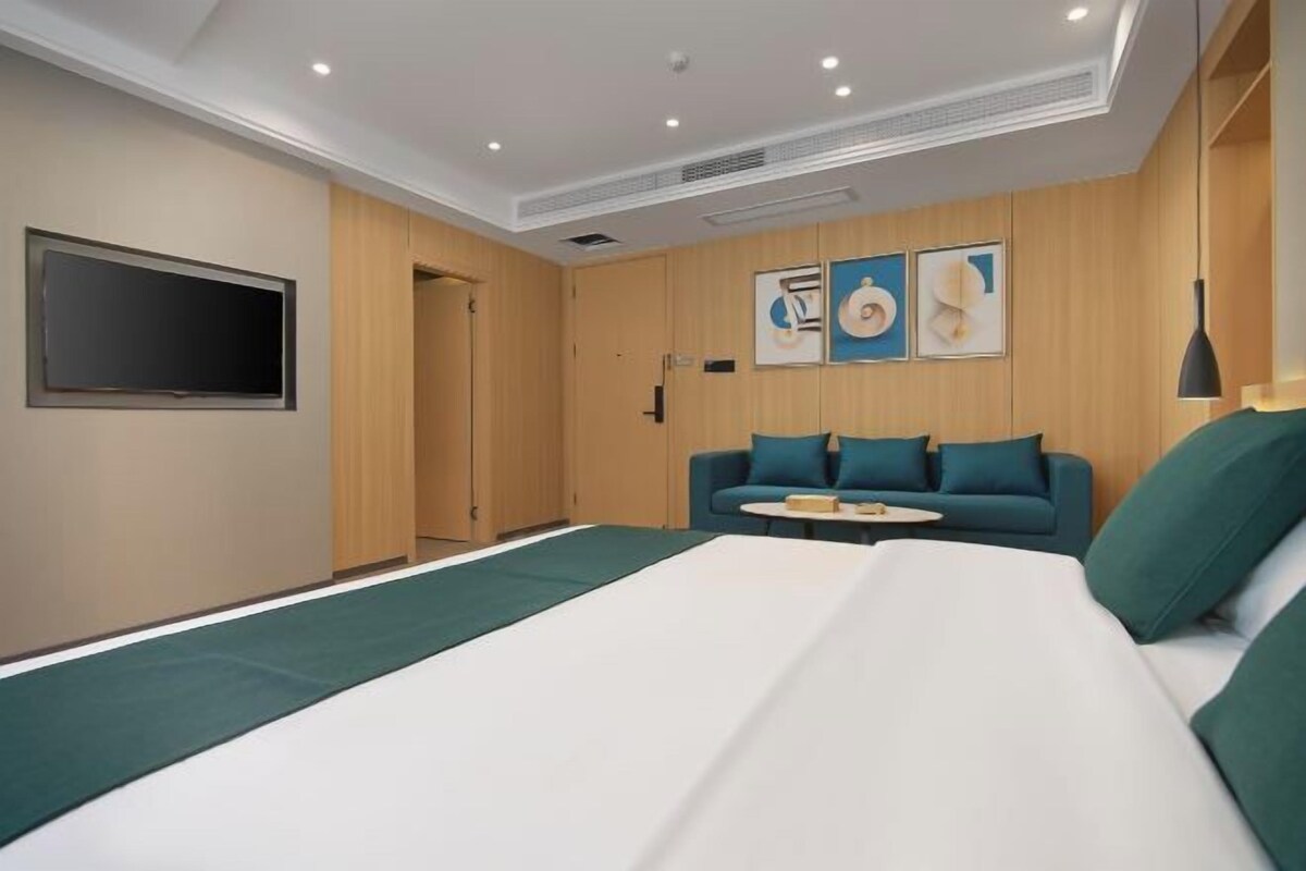A modern hotel room with a large bed, a sofa, and a TV mounted on the wall.
