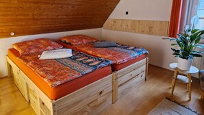 Un dormitorio acogedor con techo inclinado, paredes de madera, cama con ropa de cama estampada, una mesita y una planta en maceta.