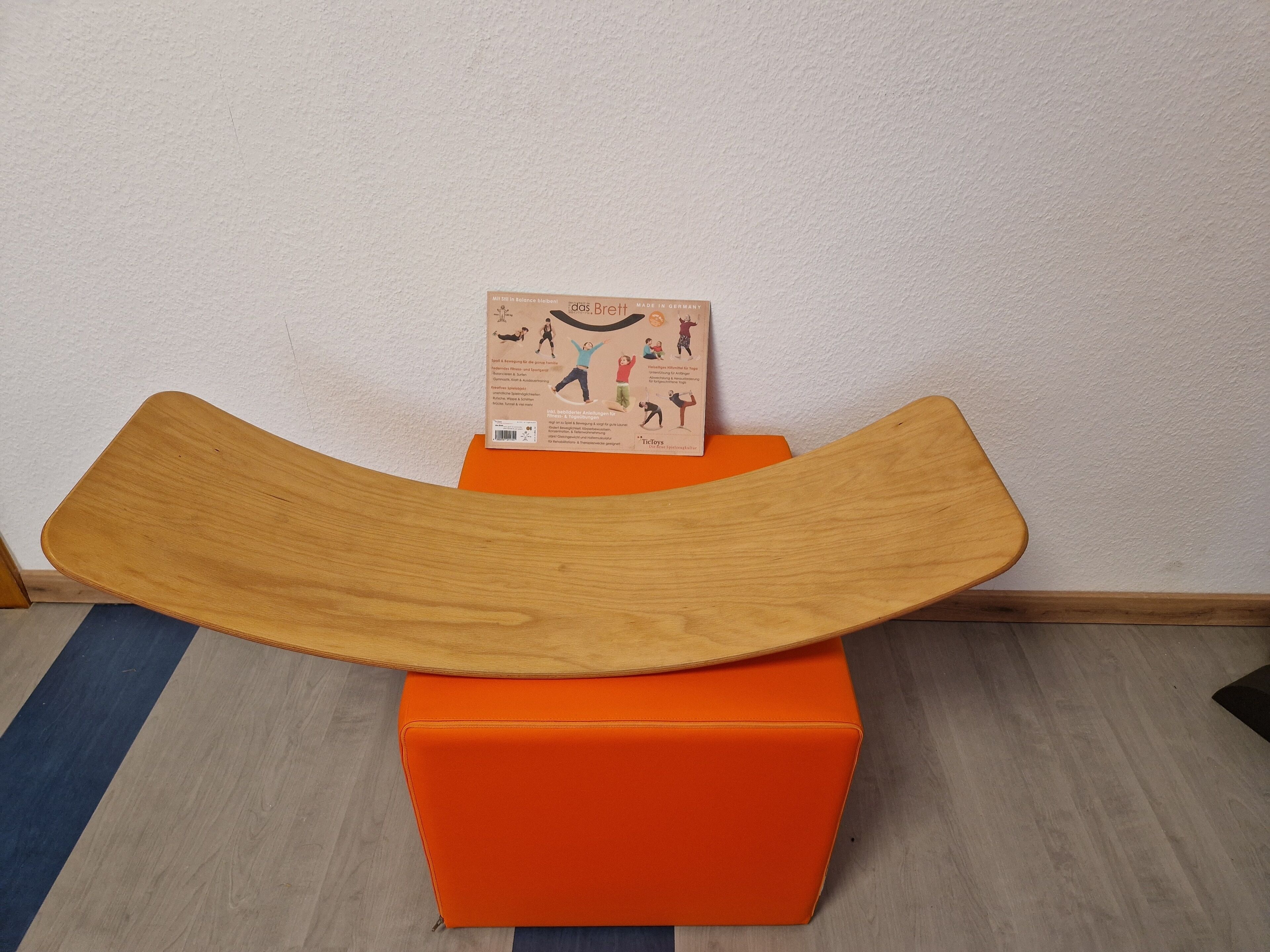 A wooden bench with a curved backrest on an orange ottoman.