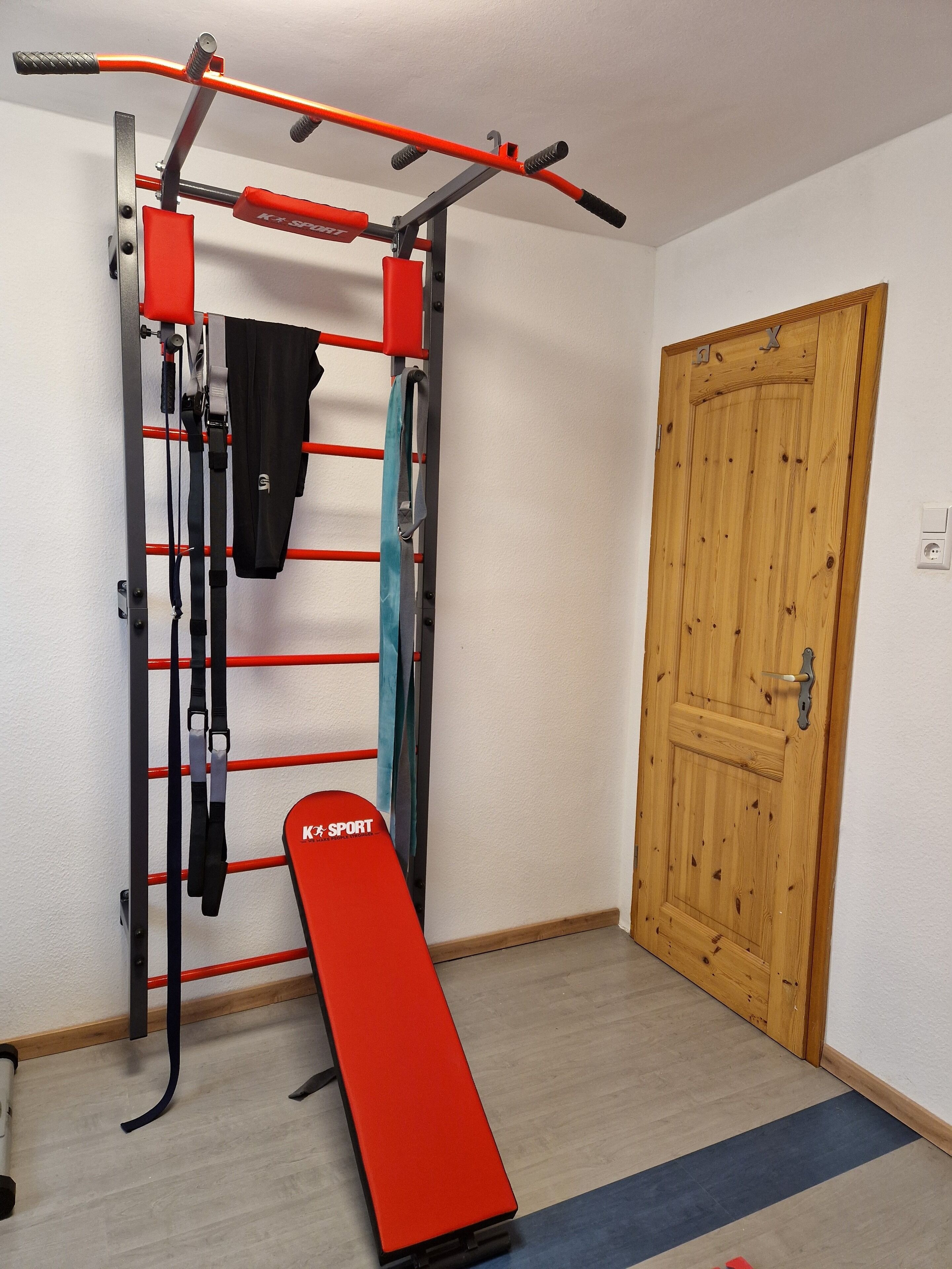 Un ensemble compact pour faire de l’exercice à la maison, comprenant une barre de traction, un banc de musculation et des bandes de résistance.