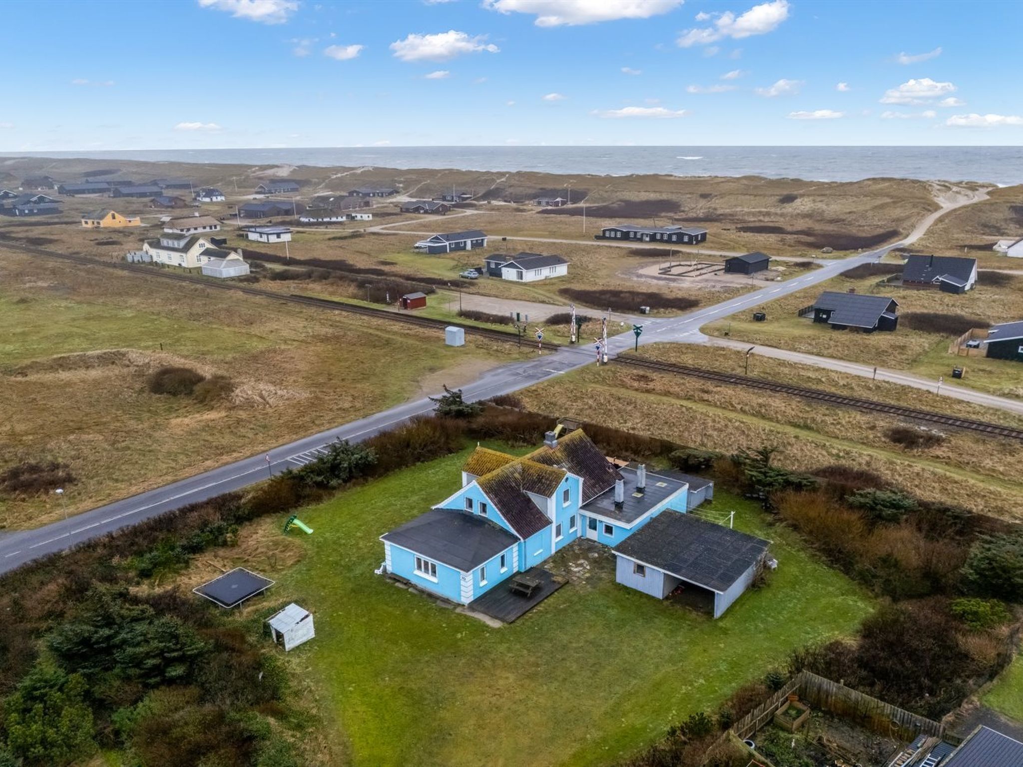 An aerial view of a coastal village with houses, a railway crossing, and a road.