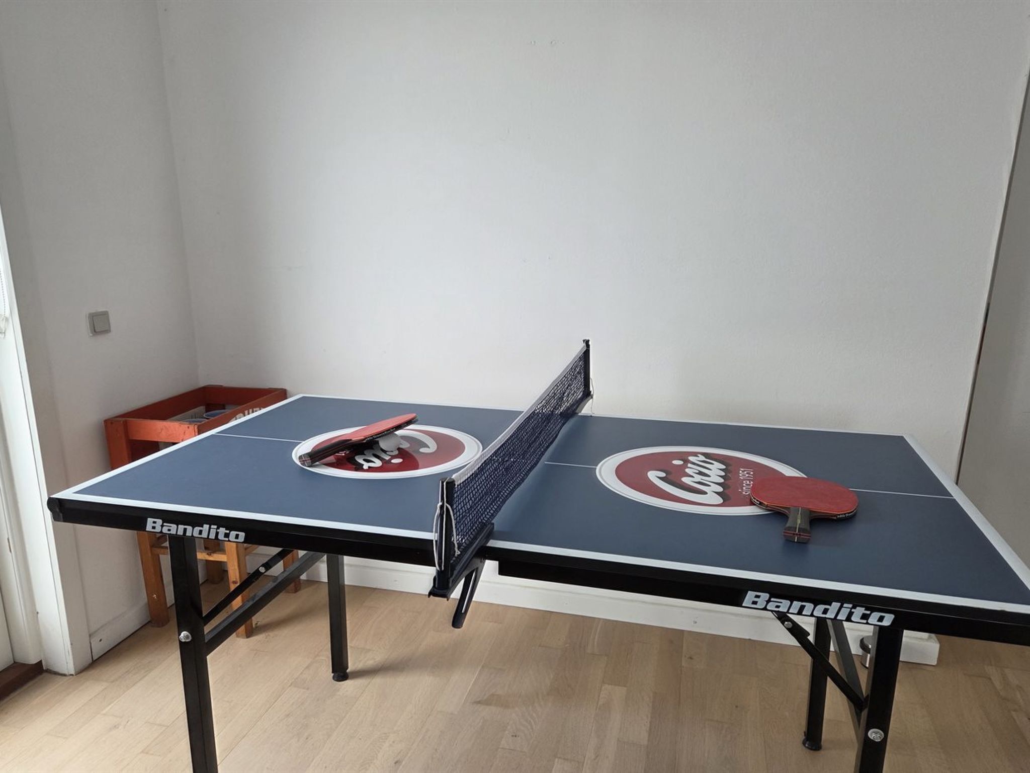 A ping pong table with a net, two paddles, and a ball.