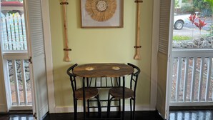 A room with a wooden table and two chairs, a framed wall art piece, and two wooden paddles on the wall. - Kona Polynesian King - Tropical Island Soul (Kailua-Kona)