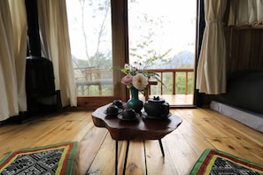 Una mesa de madera con teteras y tazas, un florero con flores y vistas al exterior a través de una ventana.