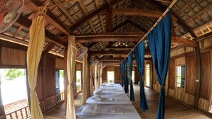 Una fila de camas individuales con sábanas y almohadas blancas, suelo de madera y techo alto con vigas a la vista.